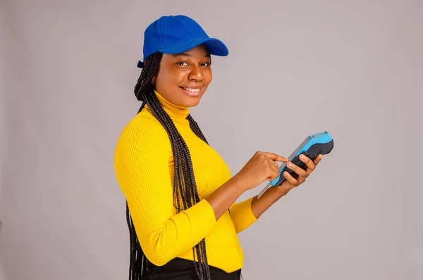 An African lady smiling and holding a payment terminal - the concept of sales