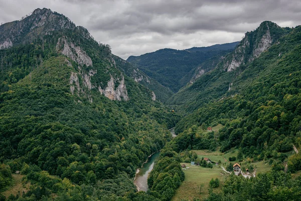 An aerial view of the lush green mountains in Montenegro with a narrow river under the cloudy sky