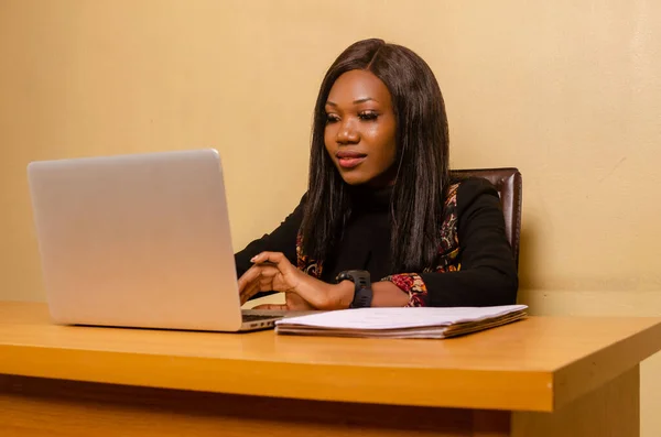 A closeup of a beautiful black woman working on her laptop at her desk with documents next to her