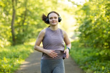 Kulaklıklı, ormanda koşan genç bir beyaz kadın.