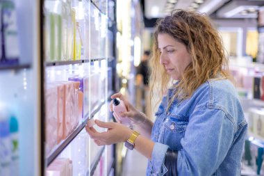 A curly haired Caucasian female checking the perfume in a perfume shop