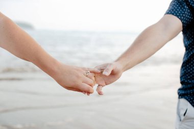 A closeup shot of hold hands of a couple standing on the new River beach in daylight in New Brunswick, Canada