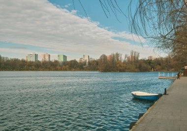 A boat on a calm blue lake surrounded with buildings and trees