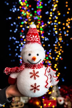 A vertical shot of a snowman Christmas plush toy against bokeh lights background