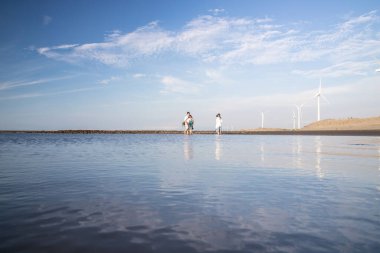 A group of people walking on a seashore with wind turbines on Caota beach in Taiwan