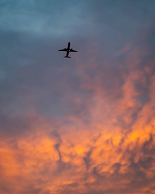 Renkli bulutlu dramatik bir gökyüzünde bir uçağın dikey alçak açılı görüntüsü.