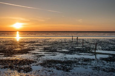 A beautiful golden sunset shining in the sky over the wavy waters at a beach in the Norddeich, Germany