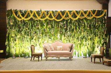 Sahnede bir kanepe ve diğer dekorlar arkasında yeşil bir perde var.