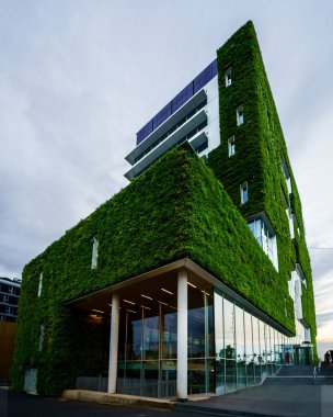 A vertical low angle of a modern-style building covered with greenery against a cloudy sky