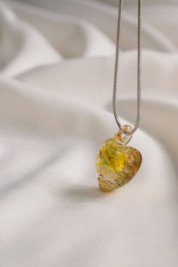 Beyaz arka planda, açık sarı el yapımı, cam kalp şeklinde bir kolyenin yakın plan çekimi.