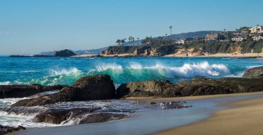 Dalgalarla dolu kayalık bir denizin ve açık gökyüzünün altında bir adanın güzel manzarası.