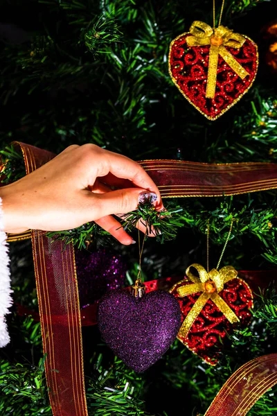 在冷杉树上挂着圣诞心形装饰品的一只雌手的垂直特写 — 图库照片
