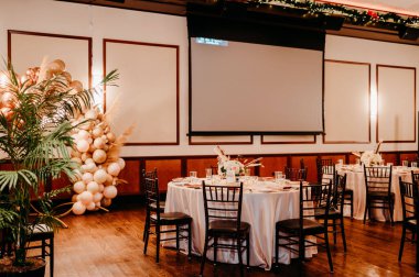 An interior of a restaurant with simple black chairs and white round tables for a birthday celebration