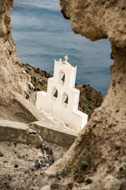 A vertical shot of three bells of Santorini on a hillside, over the background of the sea