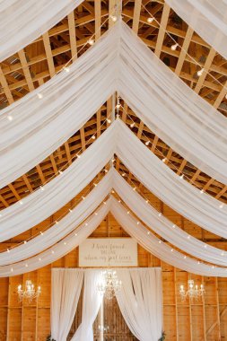 A beautiful shot of white curtains hanging on a wooden suspended ceiling with yellow lights, a wedding decor concept
