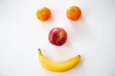 A smiley face made with banana, orange and apple on white background