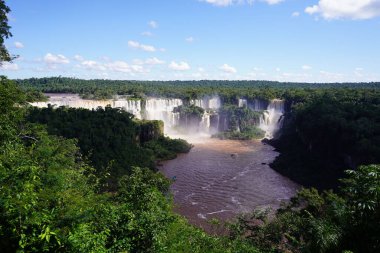 Iguazu 'nun soluk kesen manzarası bulutlu bir gökyüzüne karşı yoğun yeşil ormanlarla çevrilidir.
