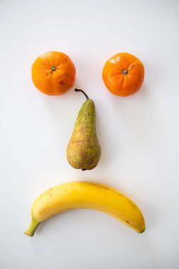 Beyaz arka planda izole edilmiş çeşitli meyvelerin dikey yakın çekimi. Üzgün bir yüz.