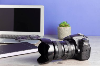 Kameralı, dizüstü bilgisayarlı, ahşap masadaki gözlüklü fotoğrafçı.