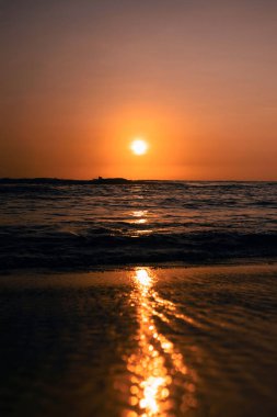 Arka planda çarpıcı bir günbatımı gökyüzü olan güzel, su sıçratan deniz dalgalarının dikey çekimi