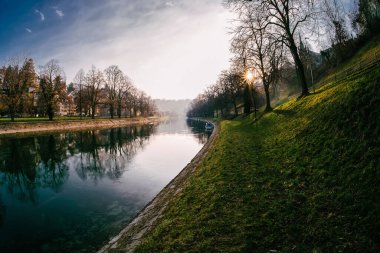 Sonbaharda ağaçlarla dolu bir parktan geçen nehrin sakin manzarası.