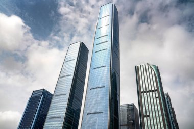 Şehir merkezinde güneşli bir günde, bulutlu gökyüzüne karşı modern gökdelenlerin alçak açılı bir görüntüsü.