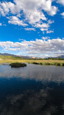 Dağlarla çevrili bulutları yansıtan bir gölün dikey görüntüsü.