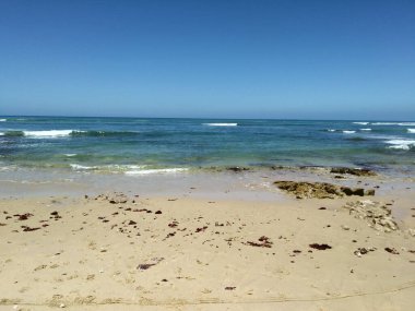 Güneşli bir günde çekilen okyanus dalgalarının arka planındaki kumlu plaj manzarası.
