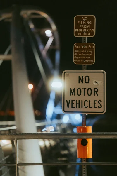 夜間の公園の歩道橋に垂直に並ぶ3つの指示標識と警告標識の垂直ショット — ストック写真