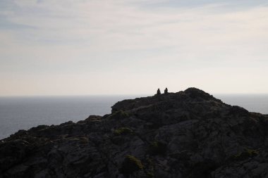Bir çift insan bir uçurumda oturup Costa Brava 'daki Cap de Creus Burnu' nun manzarasını seyrediyor.