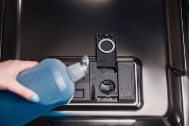 Bulaşık makinesine deterjan döken bir kadının yakın çekimi.