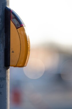A vertical selective focus shot of a yellow pedestrian walking button on a metal pole