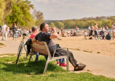 A man sitting on a wooden bench and drinking beer on a sunny spring day in Poznan, Poland