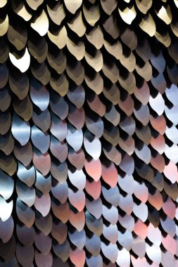 A vertical shot of metal scales reflecting different colors. A background for decoration