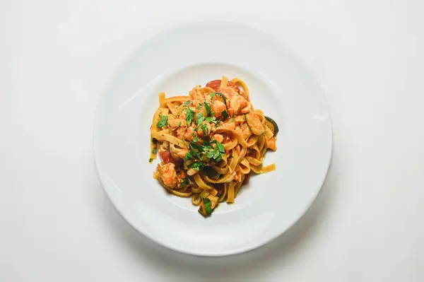 在白色桌子上的白盘上放着酱汁和青菜的意大利面的顶部视图 — 图库照片