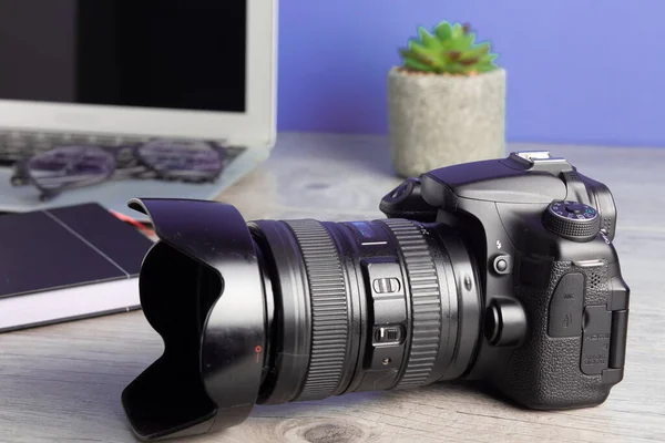 Kameralı, dizüstü bilgisayarlı, ahşap masadaki gözlüklü fotoğrafçı.