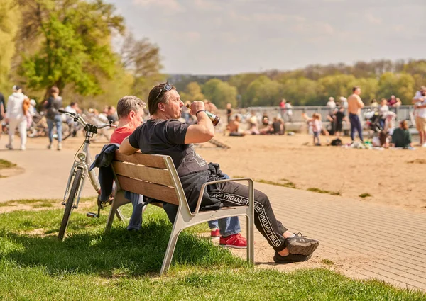 A man sitting on a wooden bench and drinking beer on a sunny spring day in Poznan, Poland