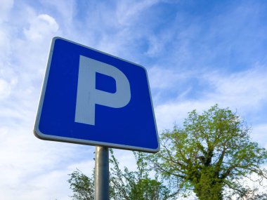 Mavi parlak gökyüzünün arka planında alçak açılı bir park işareti.