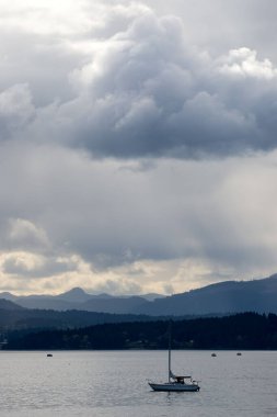 A vertical shot of a sailboat under a cloudy sky at Patricia Bay, North Saanich, Canada