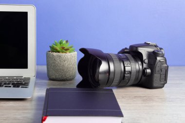 Kameralı, dizüstü bilgisayarlı, ahşap masada saksı bitkisi olan fotoğrafçı.