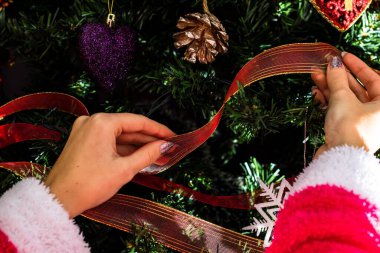 A closeup of female hands decorating a Christmas tree with a ribbon