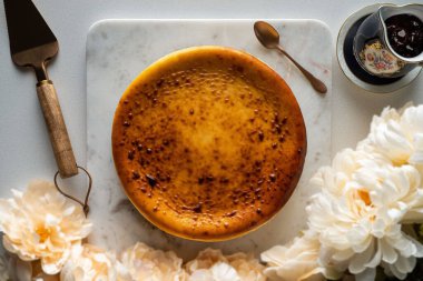 A top view of a round classic cheesecake on a marble cake stand surrounded by cutlery and flowers