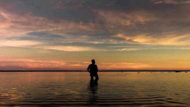 A silhouette of man in the water against a scenic sunset