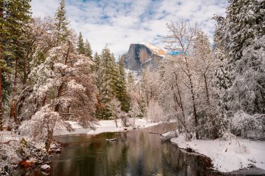 A beautiful view of rocky cliffs with snow on pond ground against a cloudy blue sky in Yosemite National Park in California, USA