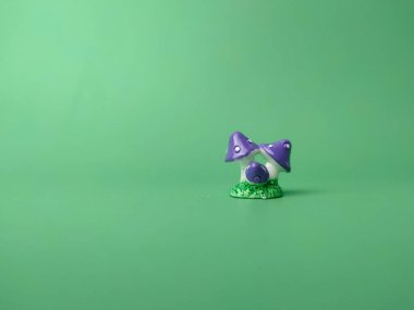 A small purple miniature mushroom isolated on a green background with copy space and text