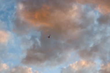looking up at helicopter against dramatic cloud formations in sky
