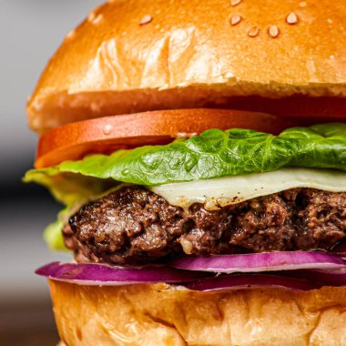 Bulanık bir arka planda izole edilmiş sulu bir hamburgerin dikey ve yakın çekimi.