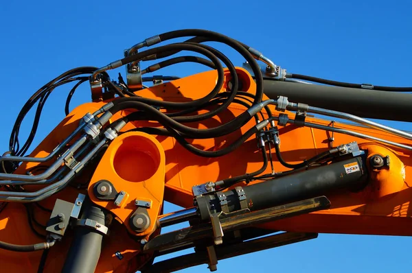 Detail of the hydraulic system of a heavy construction machine. Cylinders and pipes in the blue sky. Beautiful play of colours.