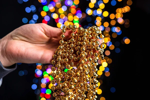 A soft focus of gold string of beads on a person\'s palm against colorful bokeh background