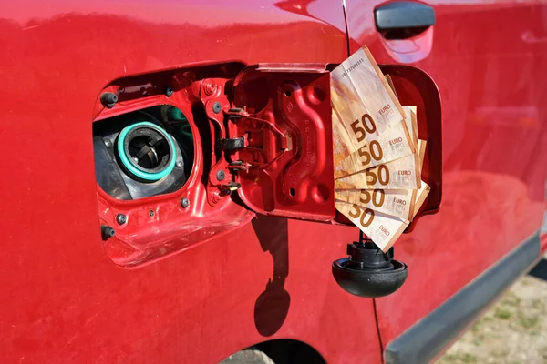 An open fuel tank of a car with a bundle of fifty euro banknotes in the lid, symbol of the rising fuel price and increasing transportation costs.